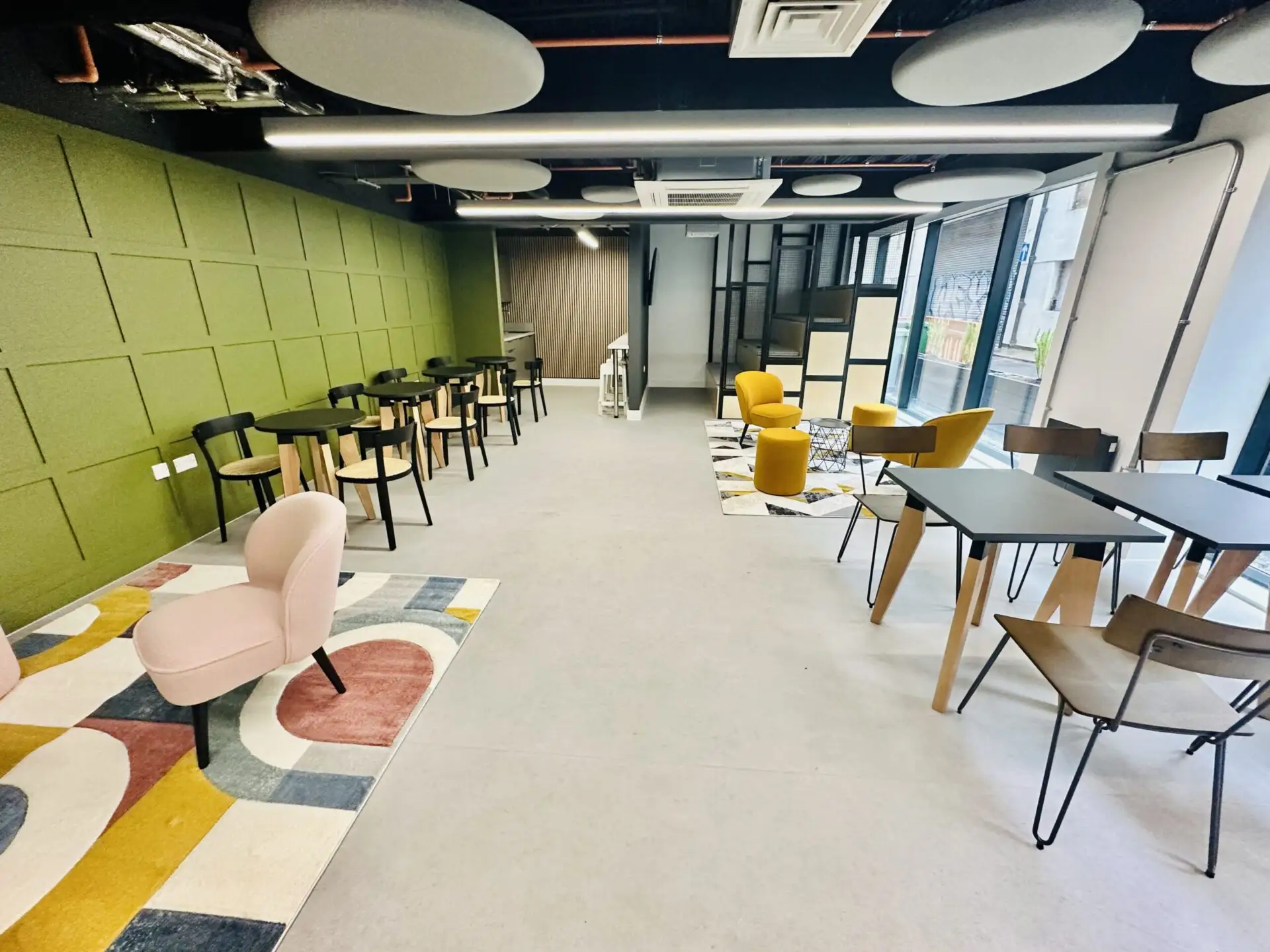 A large communal area, there are lots of tables with chairs around them. The room is light and spacious.
