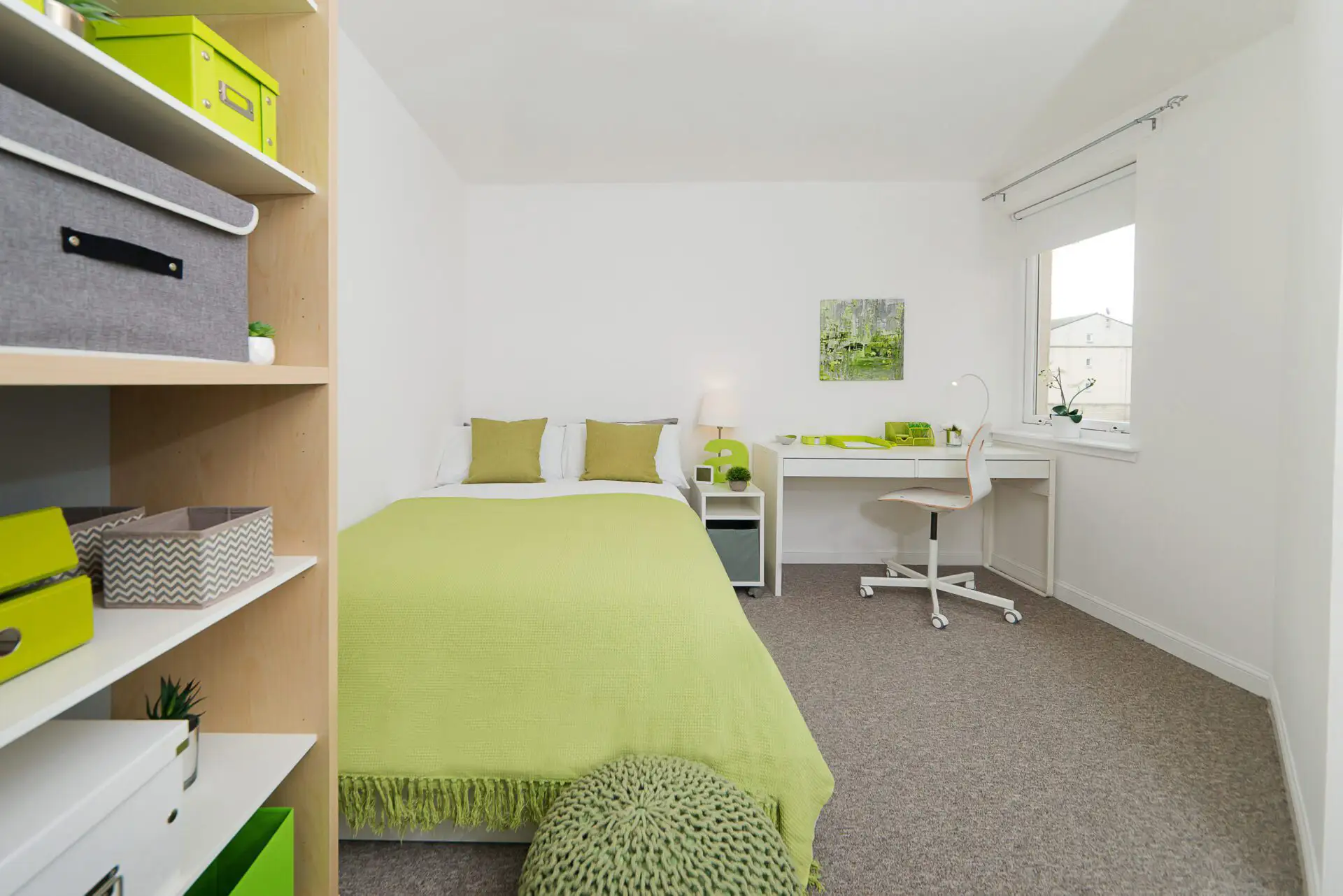 A large bedroom. The furnishings are a nice bright green. There is a 3/4 size bed, a work desk with chair and storage space.
